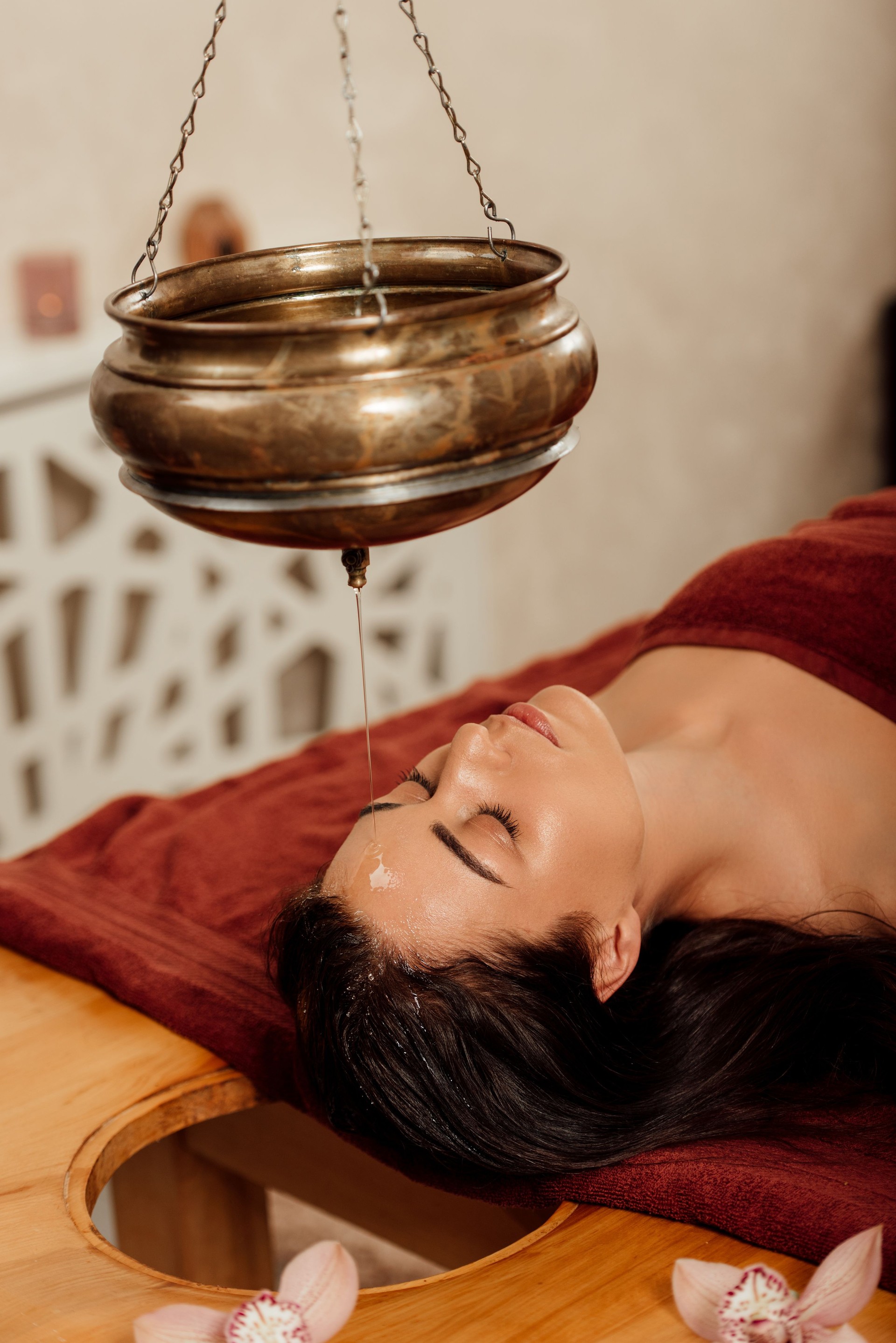 relaxed young woman lying under shirodhara vessel during ayurvedic procedure