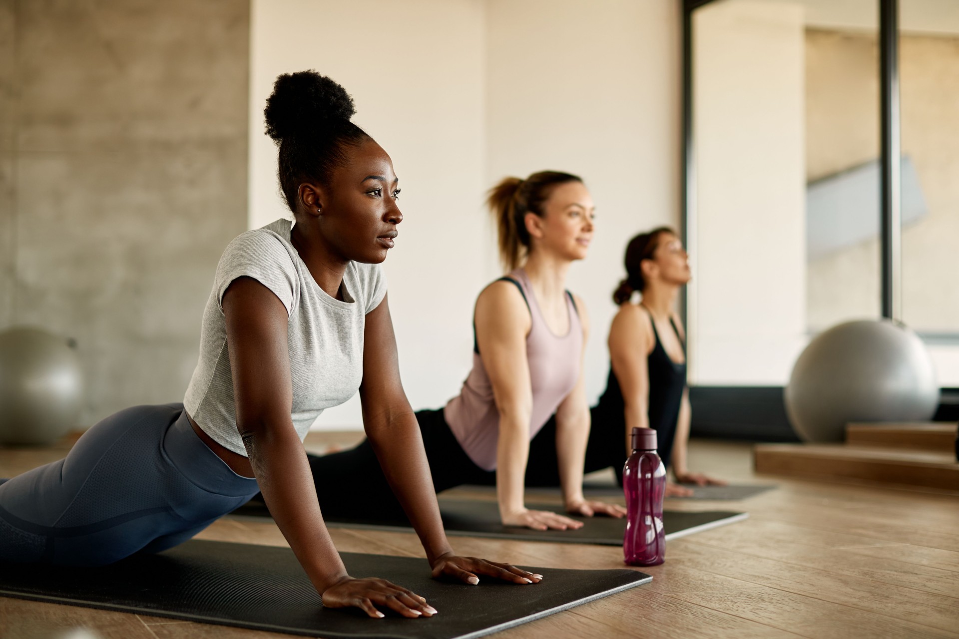 Black female athlete doing stretching exercises while warming up with group of women at health club.